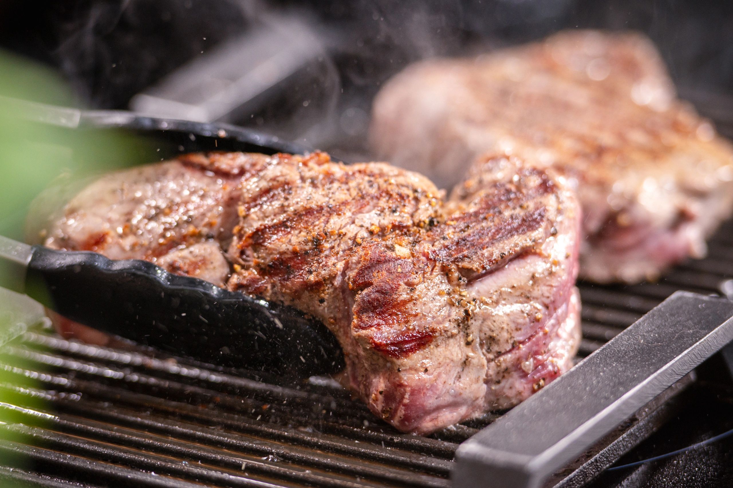 Steak cooking on a hot grill with tongs